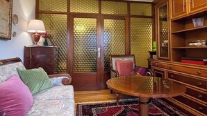 A room with a sofa, a round table, a chair, a cabinet, and a large window with a patterned curtain. - Elegante apartamento con vistas al puerto (Santander)