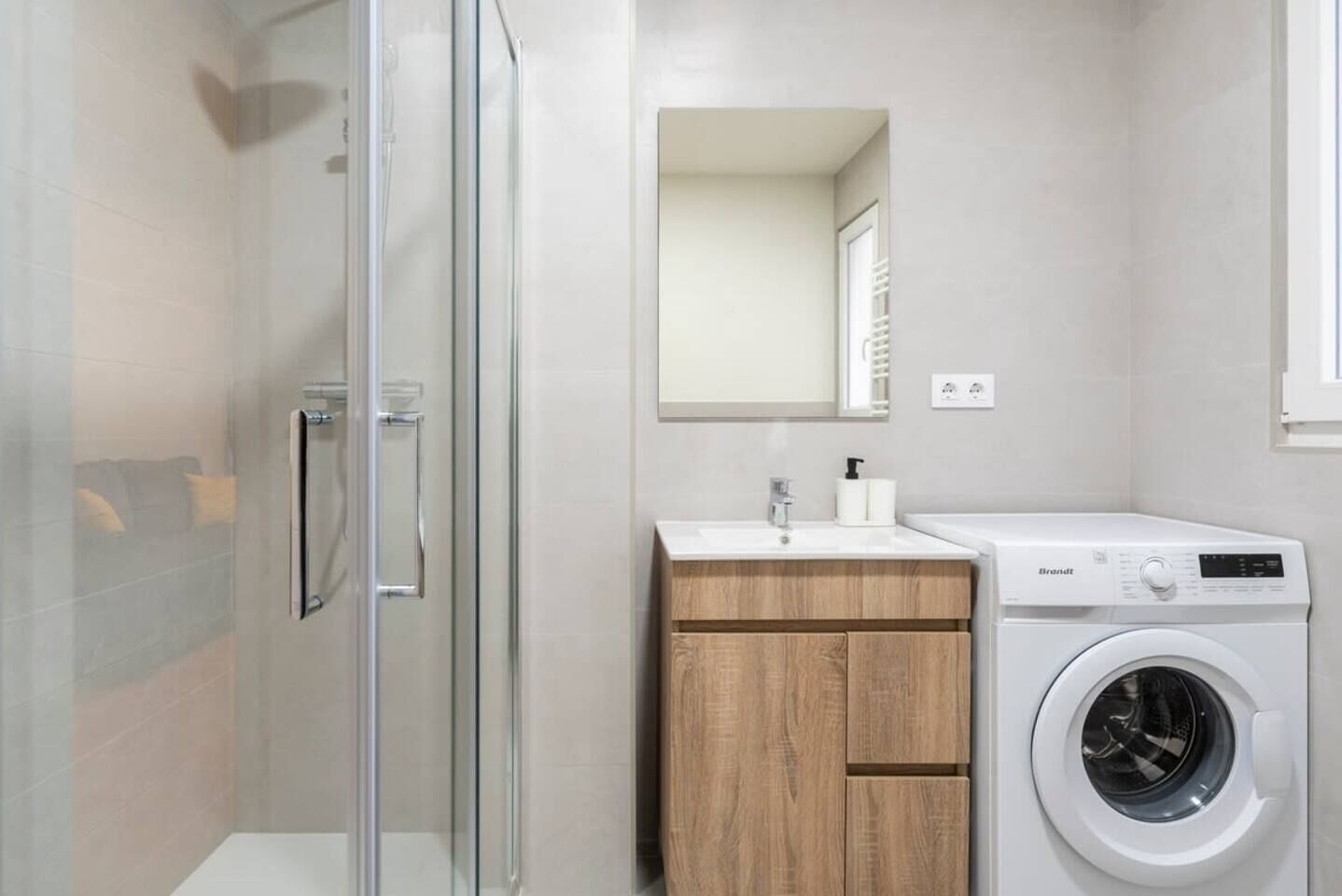 Een moderne badkamer met een douchecabine van glas, een houten wastafelmeubel, een witte wastafel en een voorlader wasmachine.