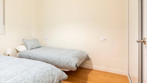 A small, clean room with two beds, a bedside table, and a wall socket. - Casa junto a la Catedral (Santander)