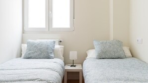 Une chambre à coucher avec deux lits, chacun recouvert d’une couvre-lit à motifs, une table de chevet avec une lampe et une fenêtre située au-dessus des lits.