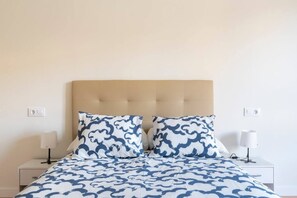 A bed with a patterned bedspread, two pillows, a tufted headboard, bedside lamps, and a nightstand with a lamp.