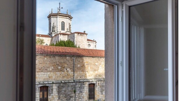 Une vue à travers la fenêtre d’un bâtiment historique doté d’un clocher et d’une façade en pierre.