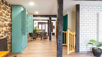 A room with a stone wall, a teal cabinet, a wooden floor, a dining area with a table and chairs, and a staircase with a wooden railing.