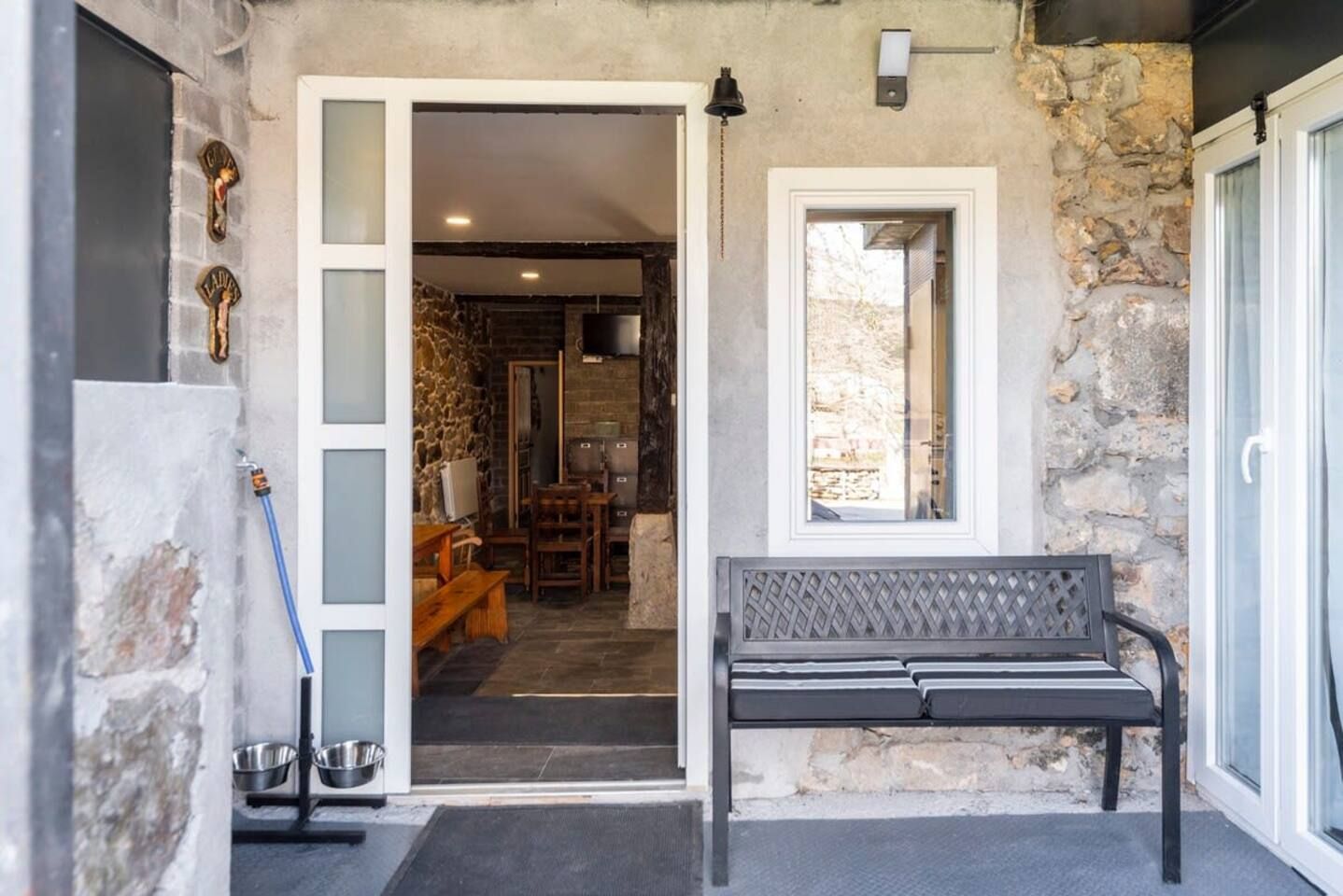 A stone exterior with a bench, a door leading to a room with a fireplace, and a window.