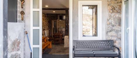 A stone exterior with a bench, a door leading to a room with a fireplace, and a window.