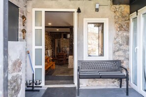 A stone exterior with a bench, a door leading to a room with a fireplace, and a window.