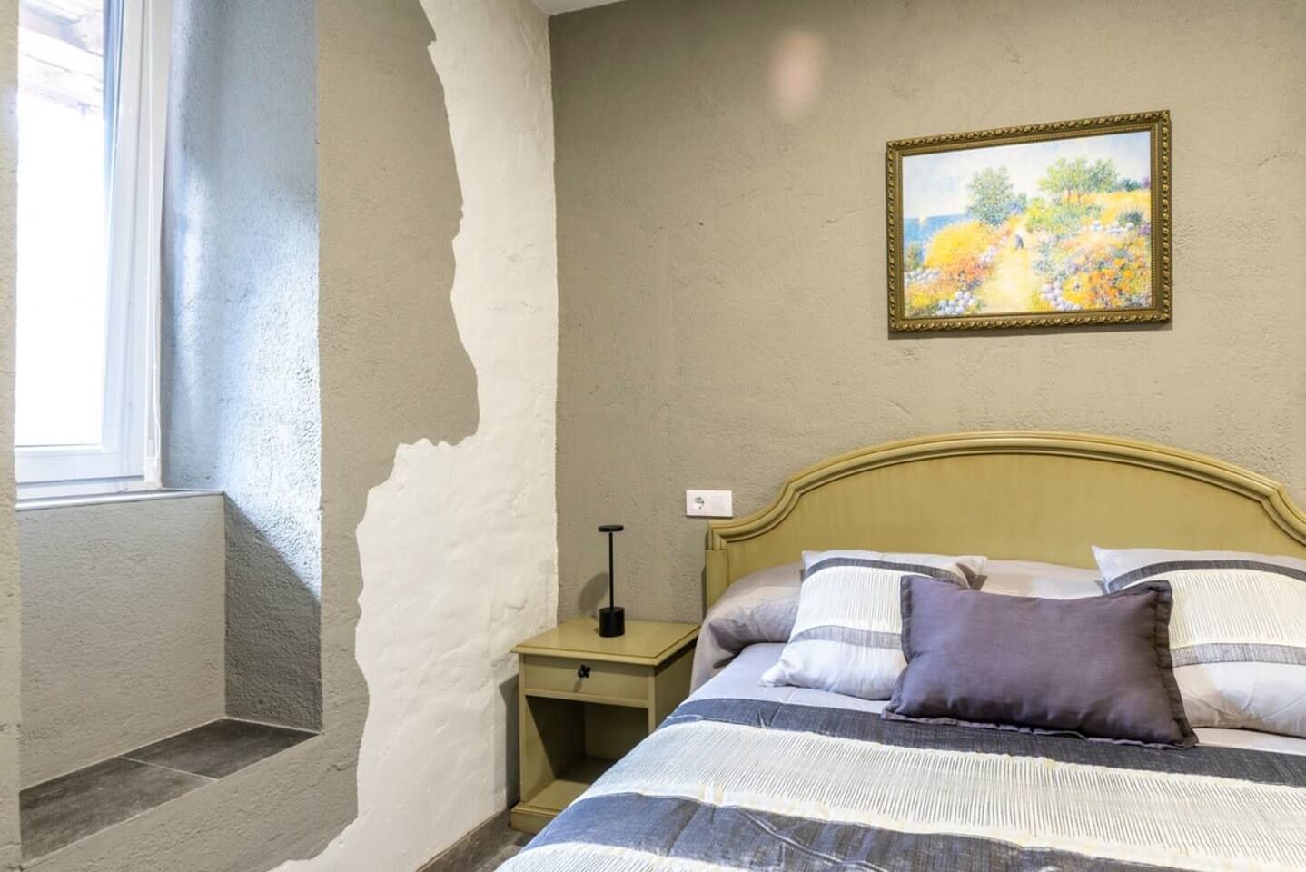 A bedroom with a bed, nightstand, and a painting on the wall.