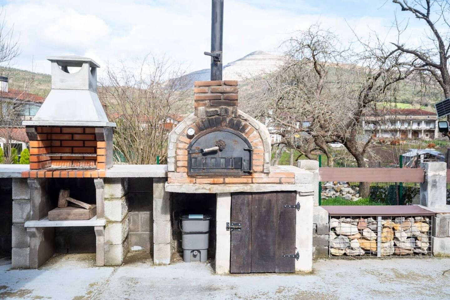Un four extérieur en briques, doté d’une cheminée, d’un banc en pierre et d’une pile de bois de chauffage.