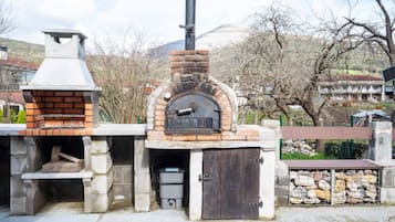 Un four extérieur en briques, doté d’une cheminée, d’un banc en pierre et d’une pile de bois de chauffage.