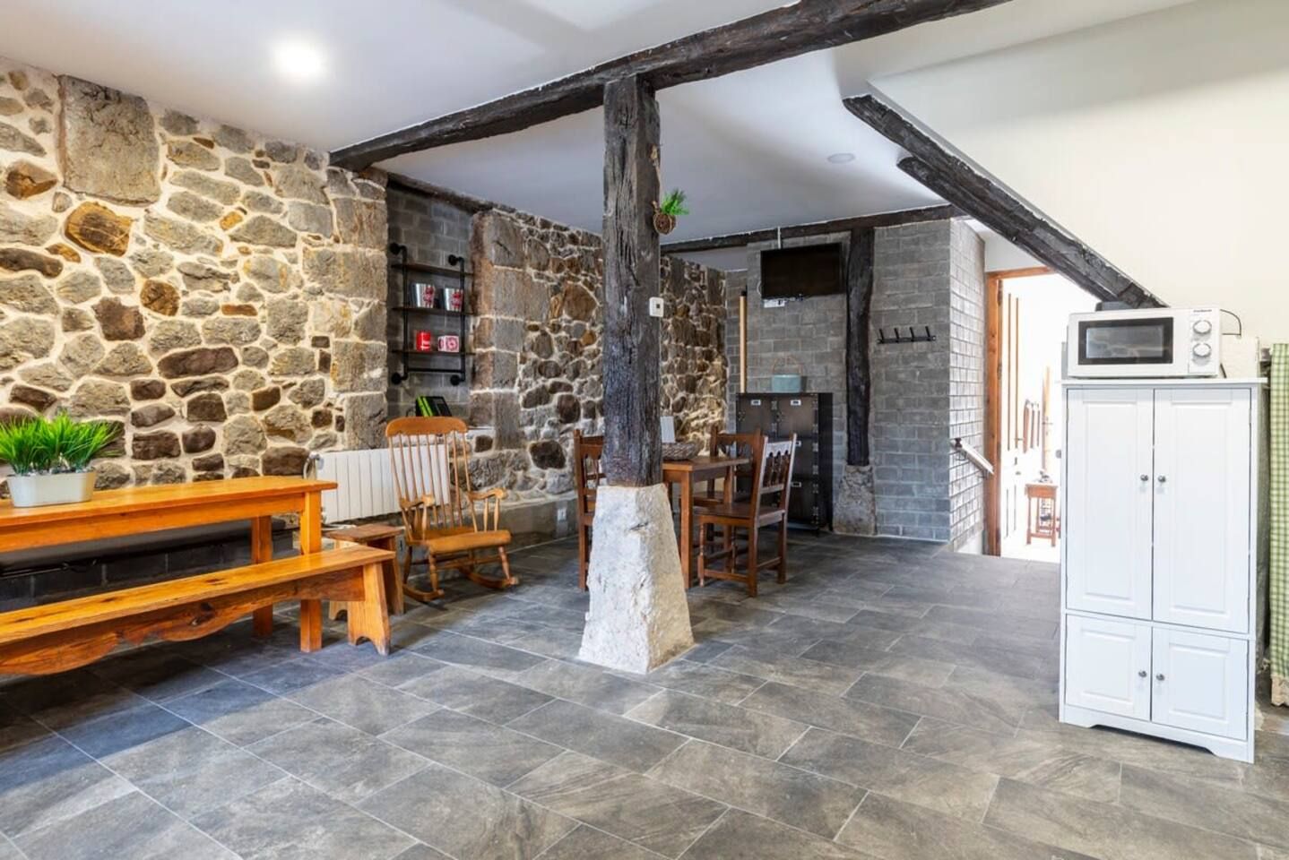 A rustic interior with stone walls, a wooden dining table, and a white cabinet.
