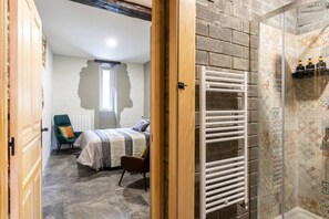 A bedroom with a bed, a chair, a radiator, and a shower area with a tiled wall. - El Cason Riva Ruesga (Riva)