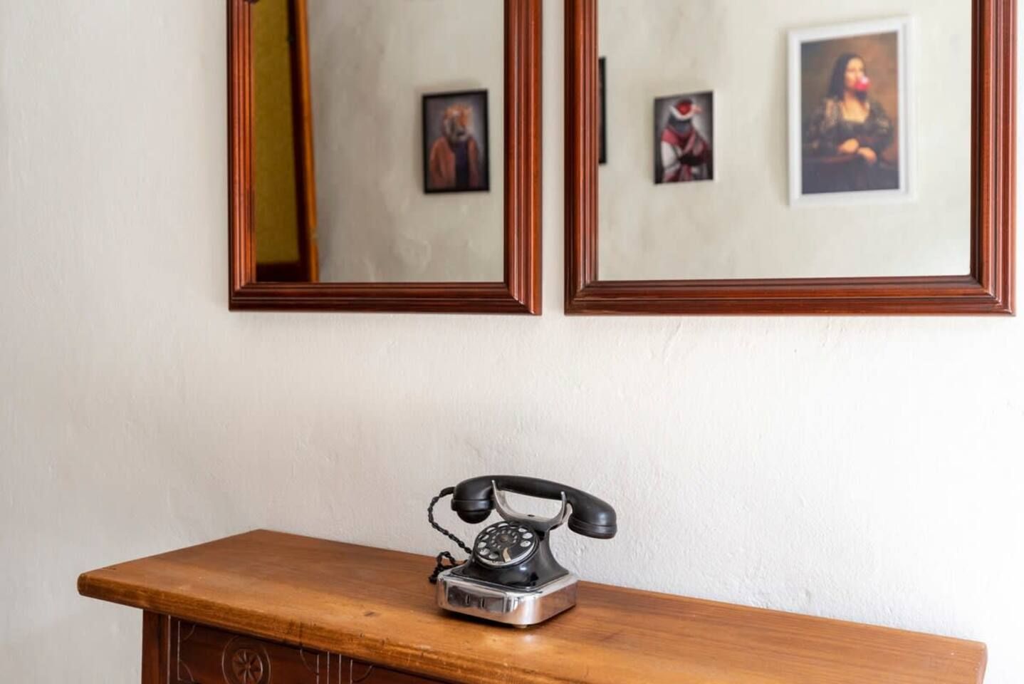 A wooden desk with a vintage telephone and two framed pictures on the wall above.