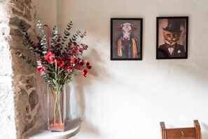 A room with a stone wall, a vase with red flowers, and two framed artworks on the wall. - El Cason Riva Ruesga (Riva)
