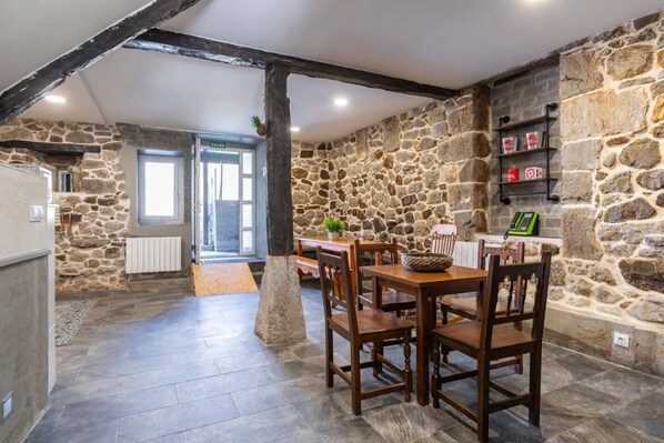 A stone-walled room with a dining table and chairs, a radiator, and a shelf with bottles. - El Cason Riva Ruesga (Riva)