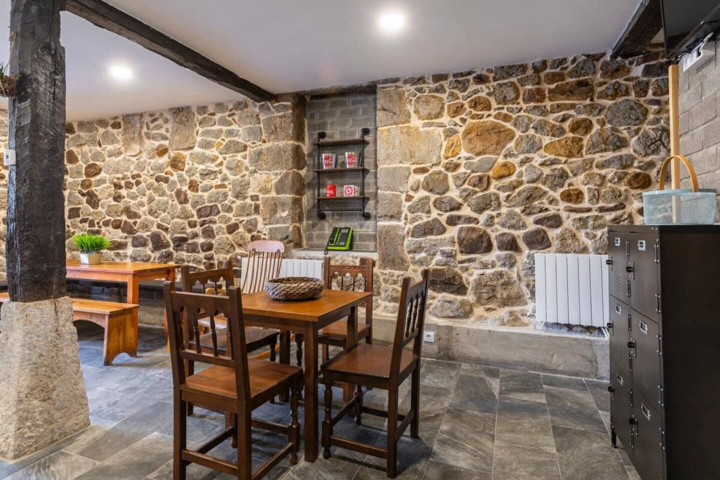 Una habitación con paredes de piedra, una mesa y sillas de madera, un banco y una chimenea.