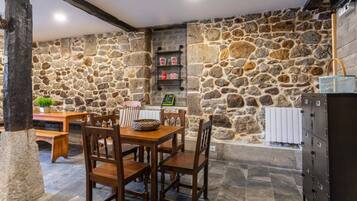 Una habitación con paredes de piedra, una mesa y sillas de madera, un banco y una chimenea.