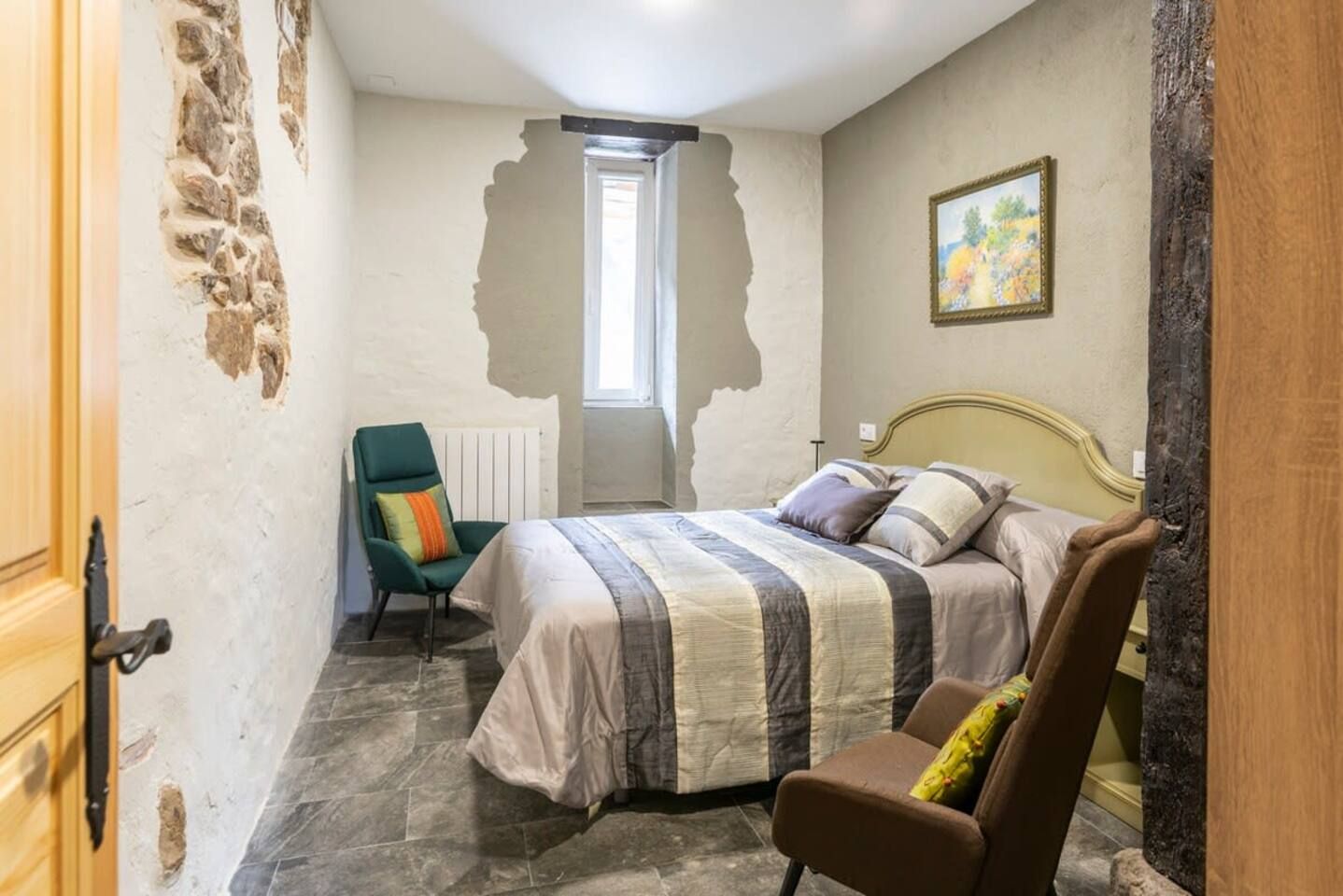 A bedroom with a bed, a chair, a radiator, and a window.