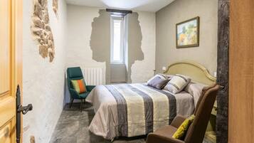 A bedroom with a bed, a chair, a radiator, and a window.