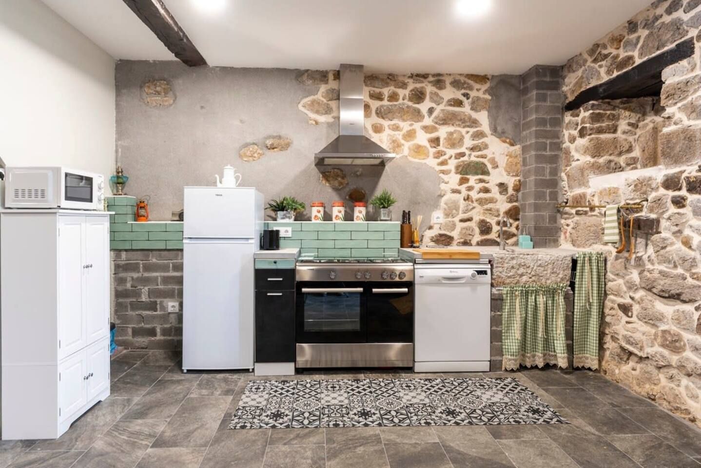 Una cocina compacta con pared de piedra, microondas, refrigerador, estufa y lavavajillas.