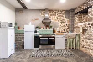 A compact kitchen with a stone wall, a microwave, a refrigerator, a stove, and a dishwasher. - El Cason Riva Ruesga (Riva)
