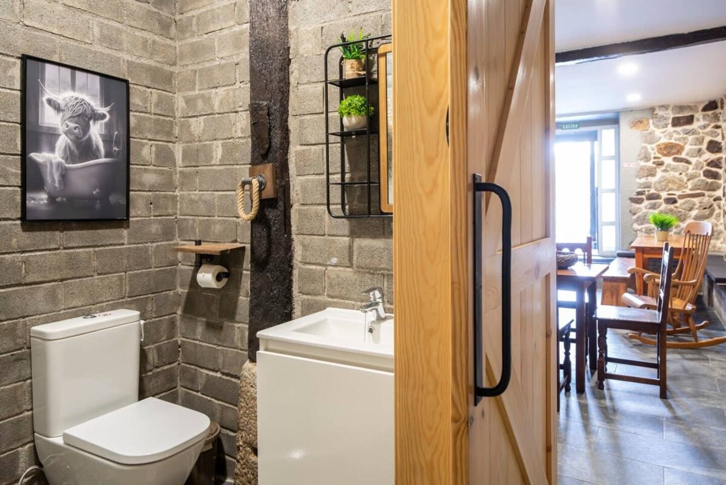 Un baño con pared de ladrillo, inodoro, lavamanos y puerta de madera.