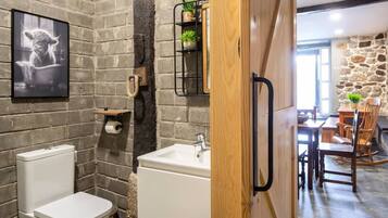 Un baño con pared de ladrillo, inodoro, lavamanos y puerta de madera.