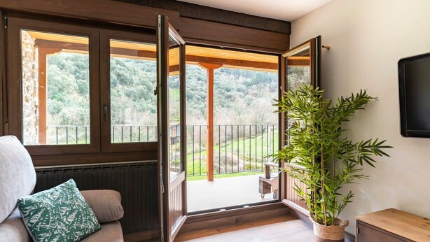 A room with a wooden floor, a sofa with a green pillow, a large bamboo plant, and a wooden cabinet.