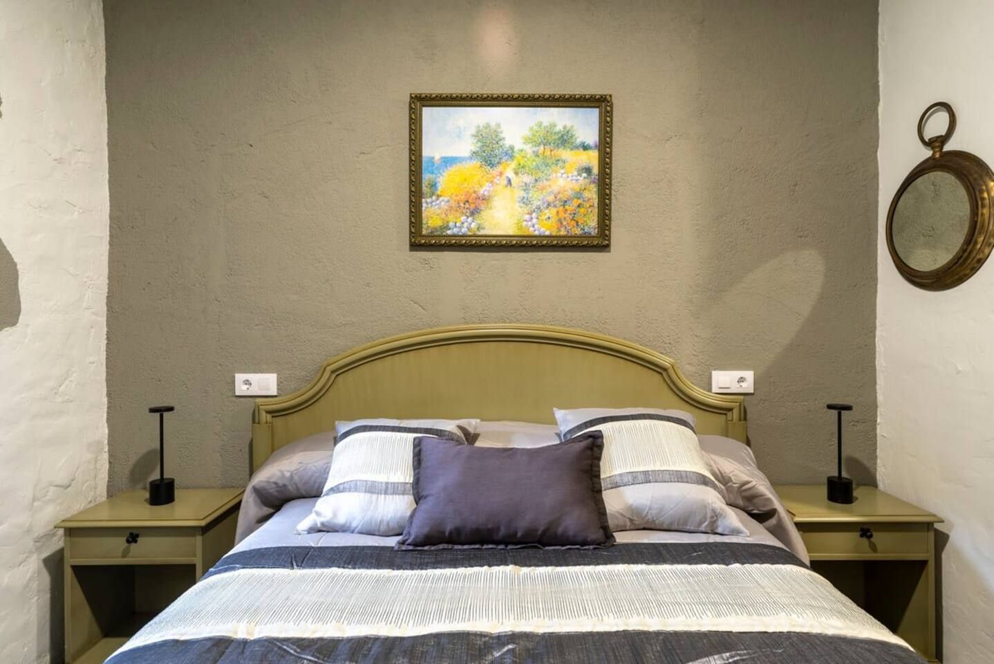 A bed with a headboard, two bedside tables, and a wall-mounted painting.