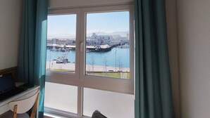 Een kamer met een groot raam met uitzicht op een jachthaven en een stadsgezicht.