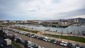 A marina with boats docked, a parking lot with cars, and industrial buildings in the background. - Sailor home Santander (Santander)