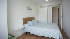 A bedroom with a bed, a nightstand, a wall-mounted shelf, a wardrobe, and a door leading to another room. - Sailor home Santander (Santander)