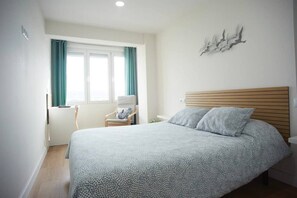 A bedroom with a bed, a chair, a window with curtains, and a wall-mounted light fixture. - Sailor home Santander (Santander)