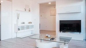 A modern living room with a glass coffee table, white entertainment unit, and a flat-screen TV. - GuestReady - Sonho dos Avós I (Câmara de Lobos)