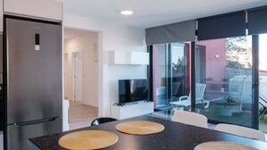 A modern kitchen with a built-in refrigerator, a dining area with a black countertop and woven placemats, and a glass door leading to an outdoor seating area. - GuestReady - Sonho dos Avós I (Câmara de Lobos)