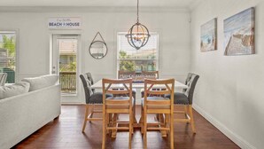 A dining area with a wooden table and chairs, a hanging light fixture, and a sign reading "Beach House".