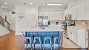 A modern kitchen with white cabinetry, a central island with bar stools, stainless steel appliances, and a tiled backsplash.