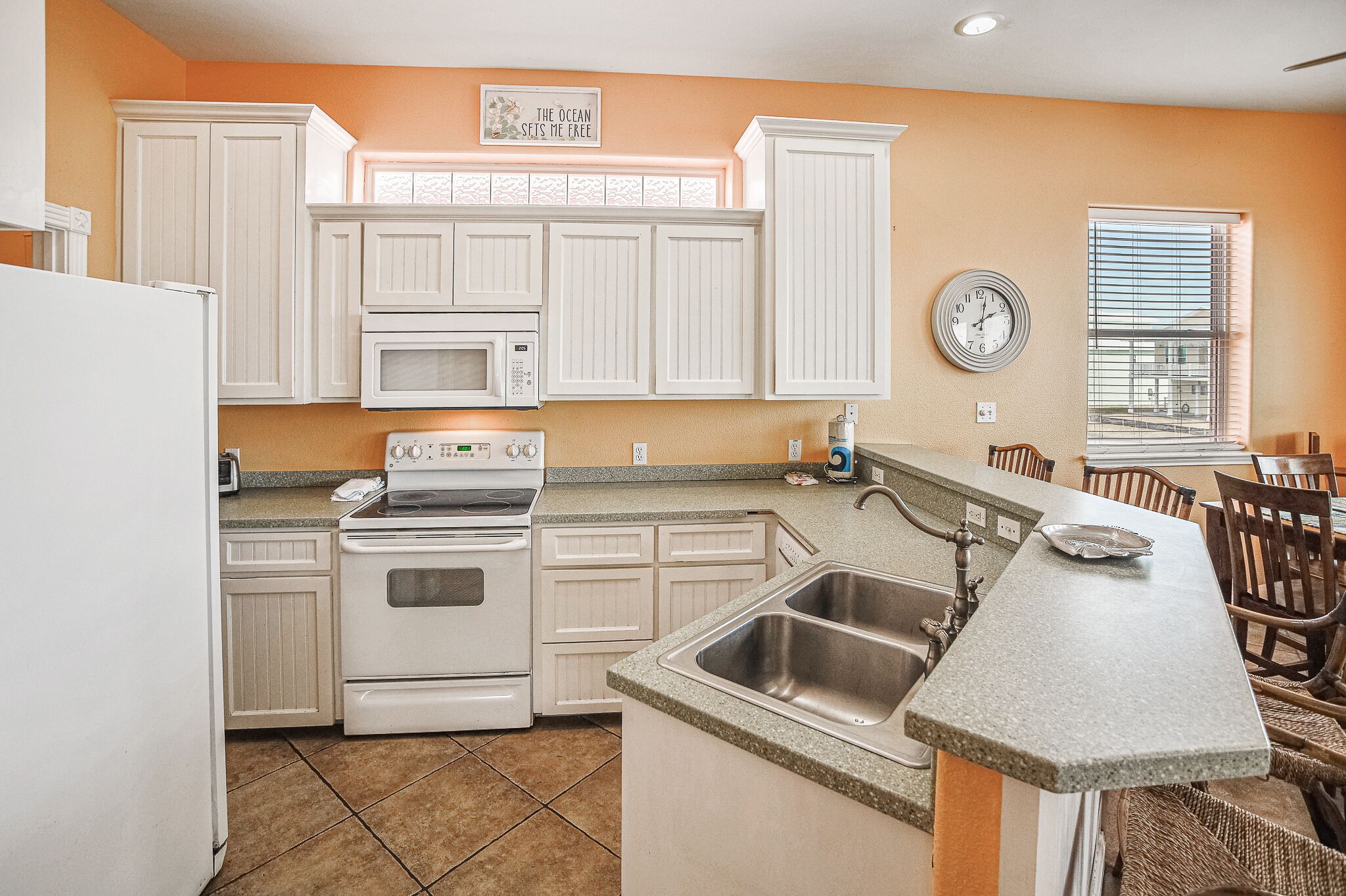 A kitchen with white cabinets, a stove, a microwave, a sink, and a dining area with chairs.