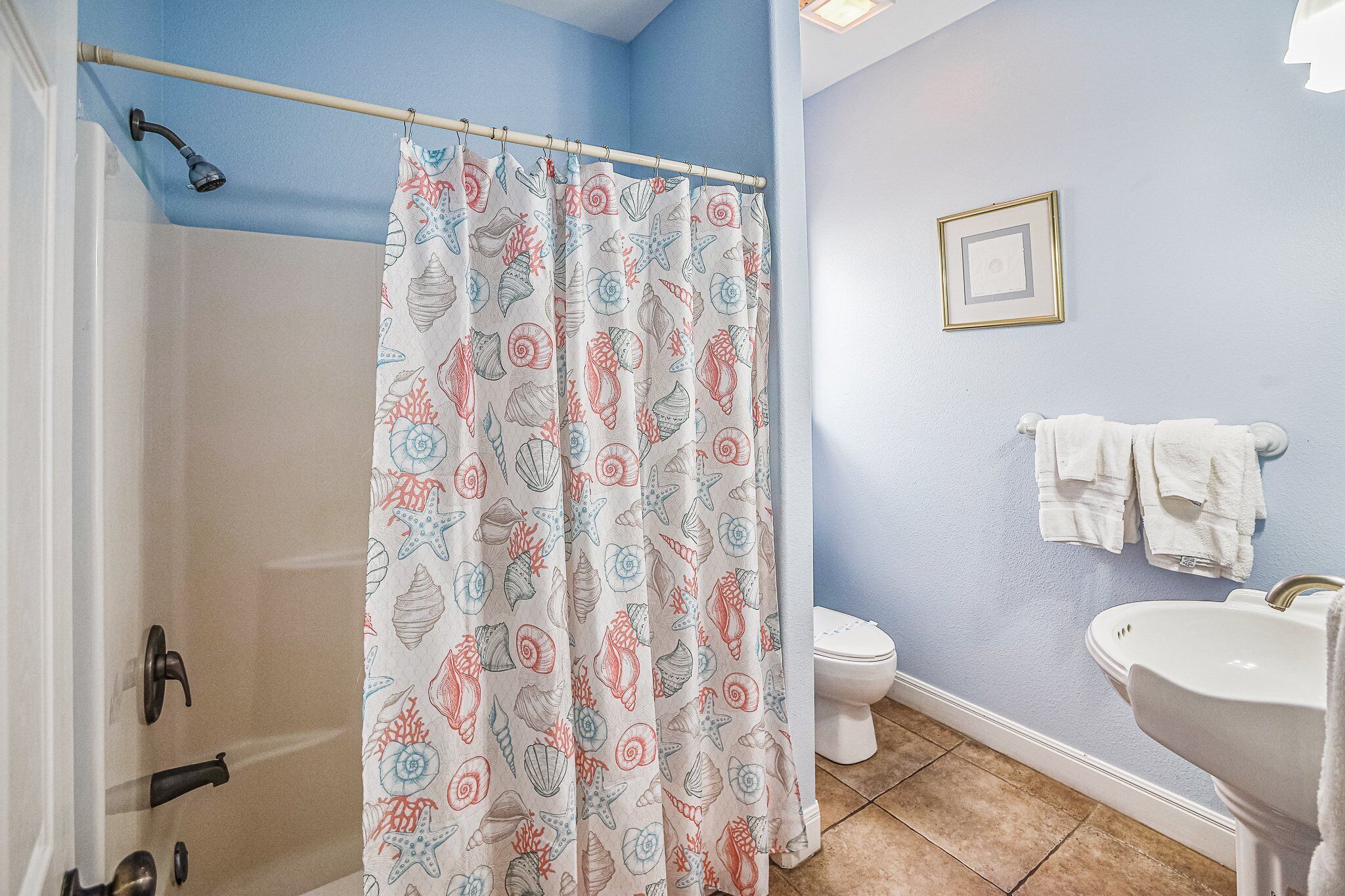 A bathroom with a shower curtain featuring a seashell pattern, a white toilet, and a white sink.