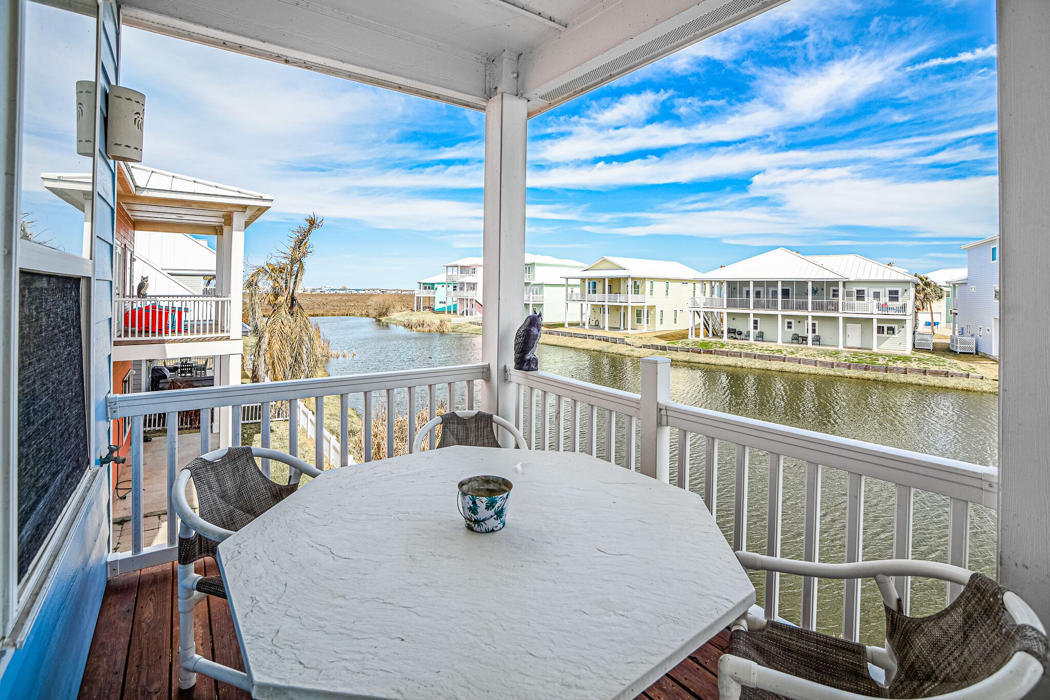 A covered balcony with a table and chairs, overlooking a river and houses.