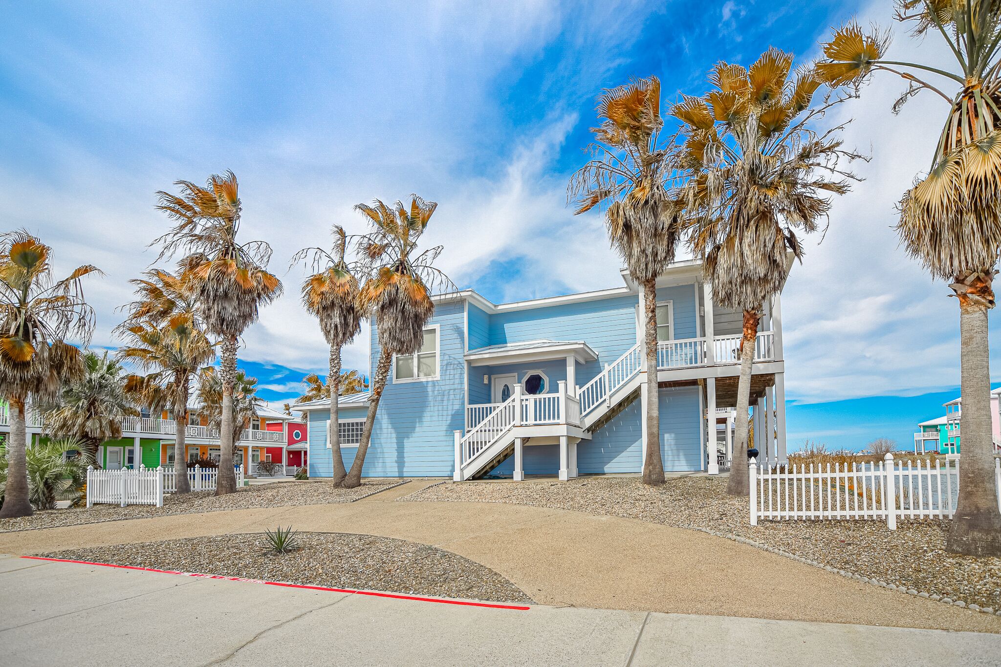 A beachfront property with a blue building, white railings, and palm trees.