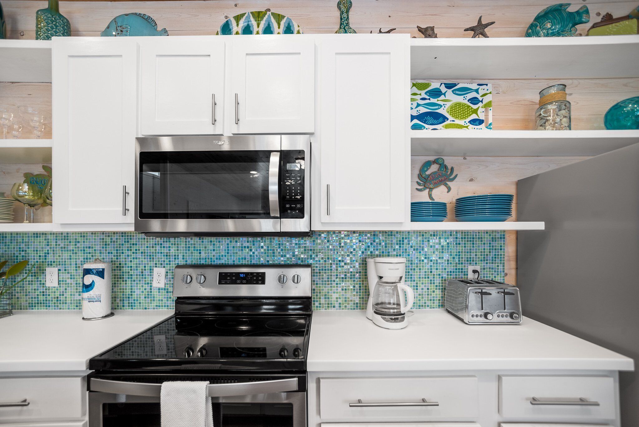 A kitchen with white cabinets, a stainless steel microwave, a stove, and a coffee maker.