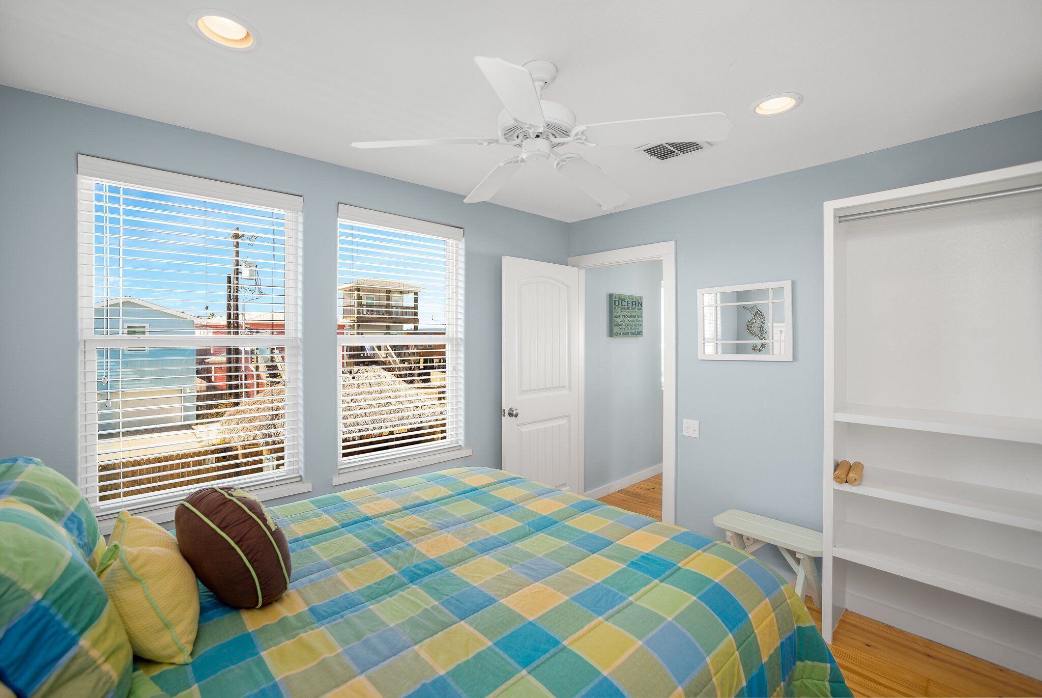 A bedroom with a bed, a ceiling fan, a window with blinds, a door, and a view of the ocean.