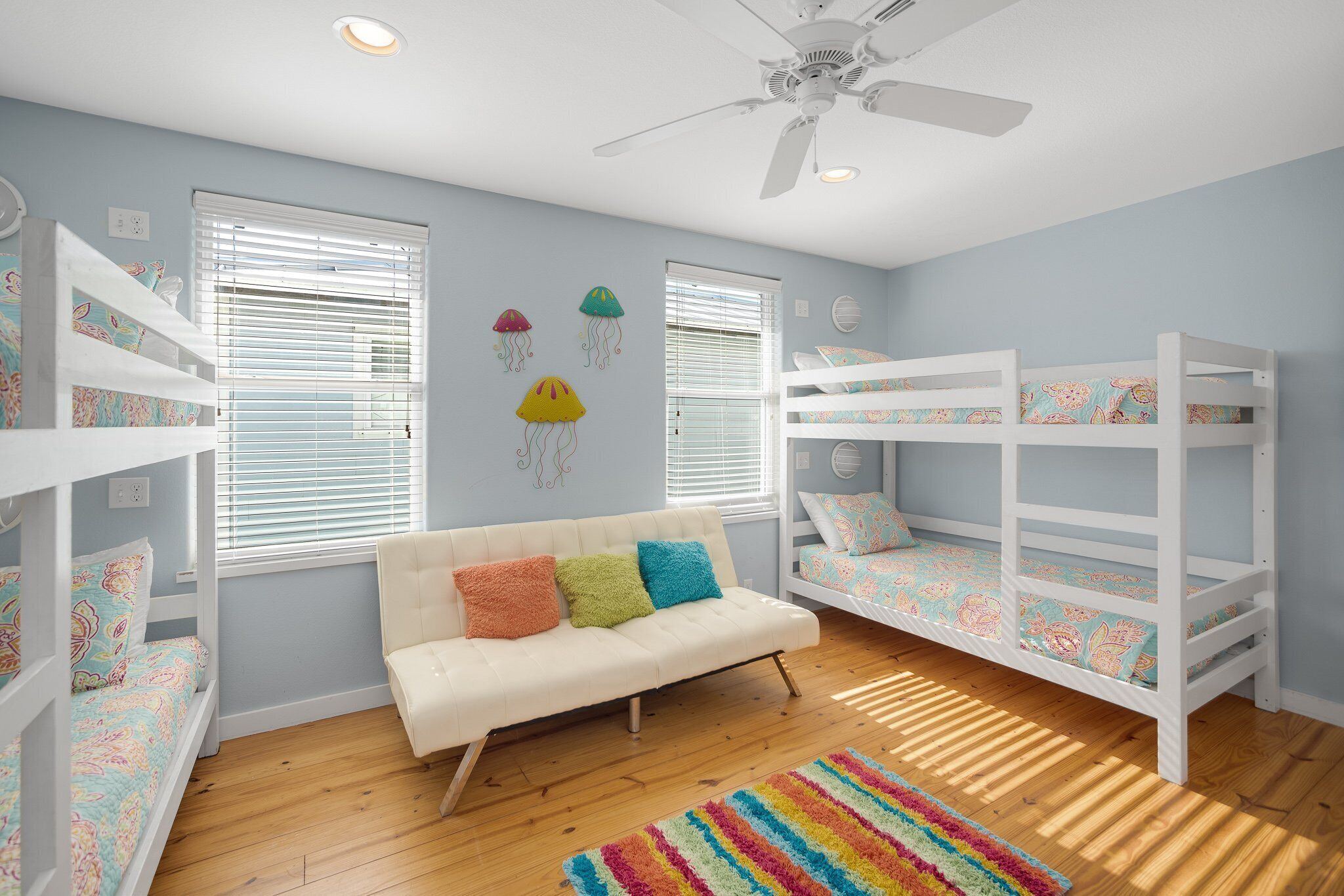 Ein Kinderzimmer mit Etagenbetten, einem weißen Sofa und einem Deckenventilator.