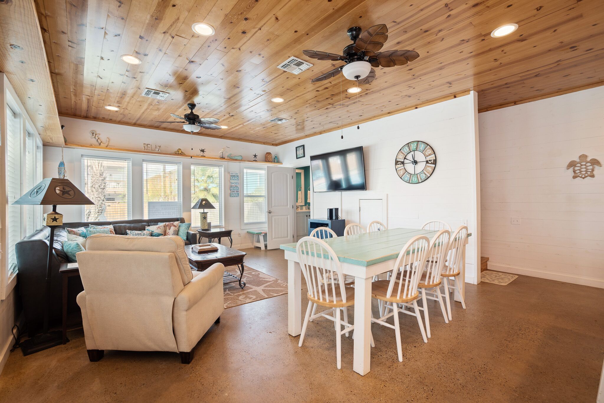 A spacious living room with a wooden ceiling, a dining area with a white table and chairs, and a TV mounted on the wall.
