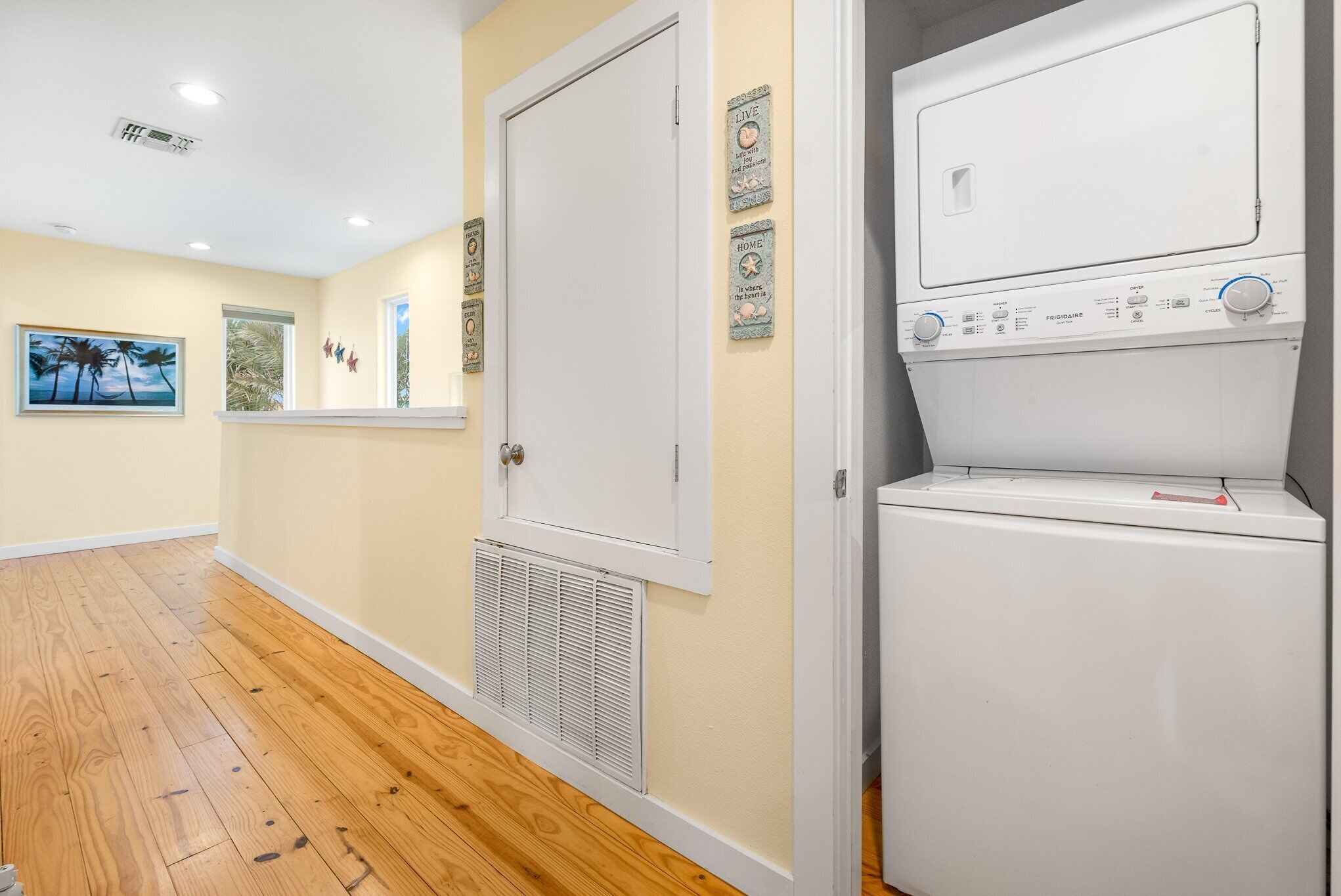 A laundry room with a front-loading washer and dryer, wooden flooring, and decorative wall art.
