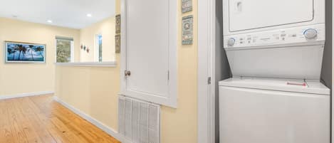 A laundry room with a front-loading washer and dryer, wooden flooring, and decorative wall art.