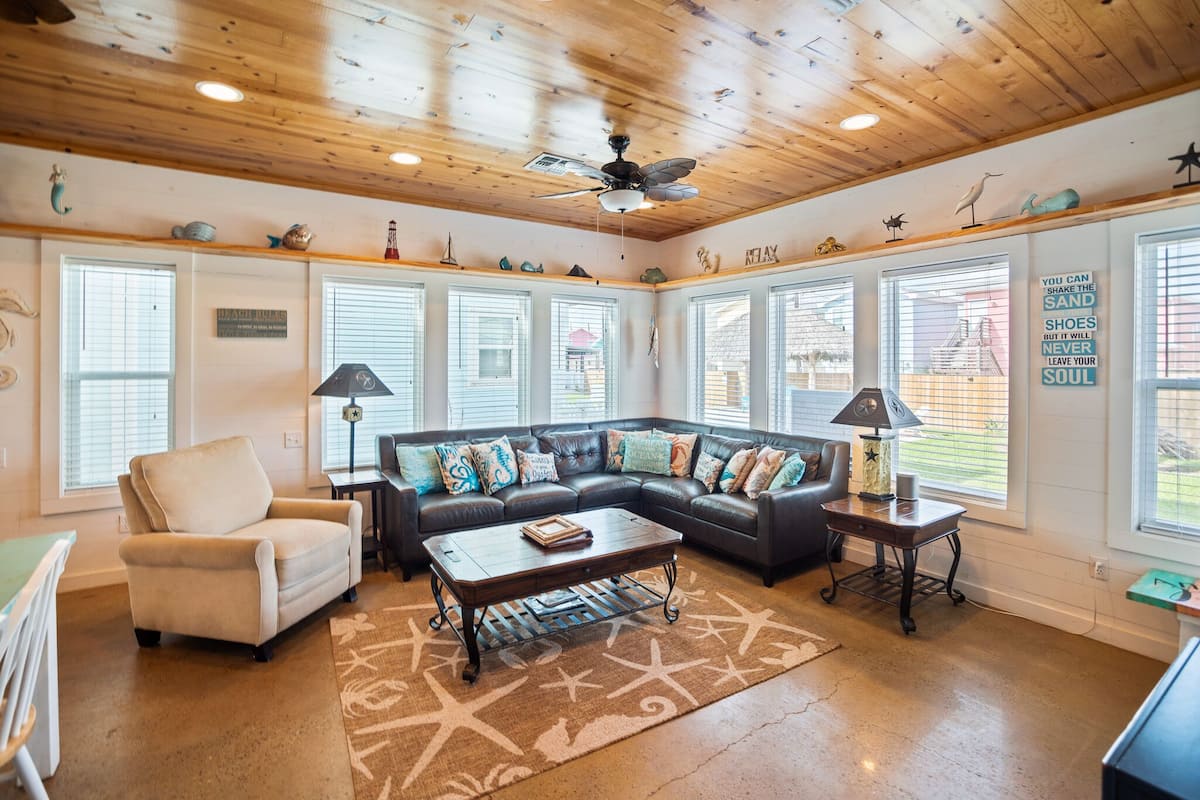A cozy living room with a sectional sofa, a coffee table, and a ceiling fan.