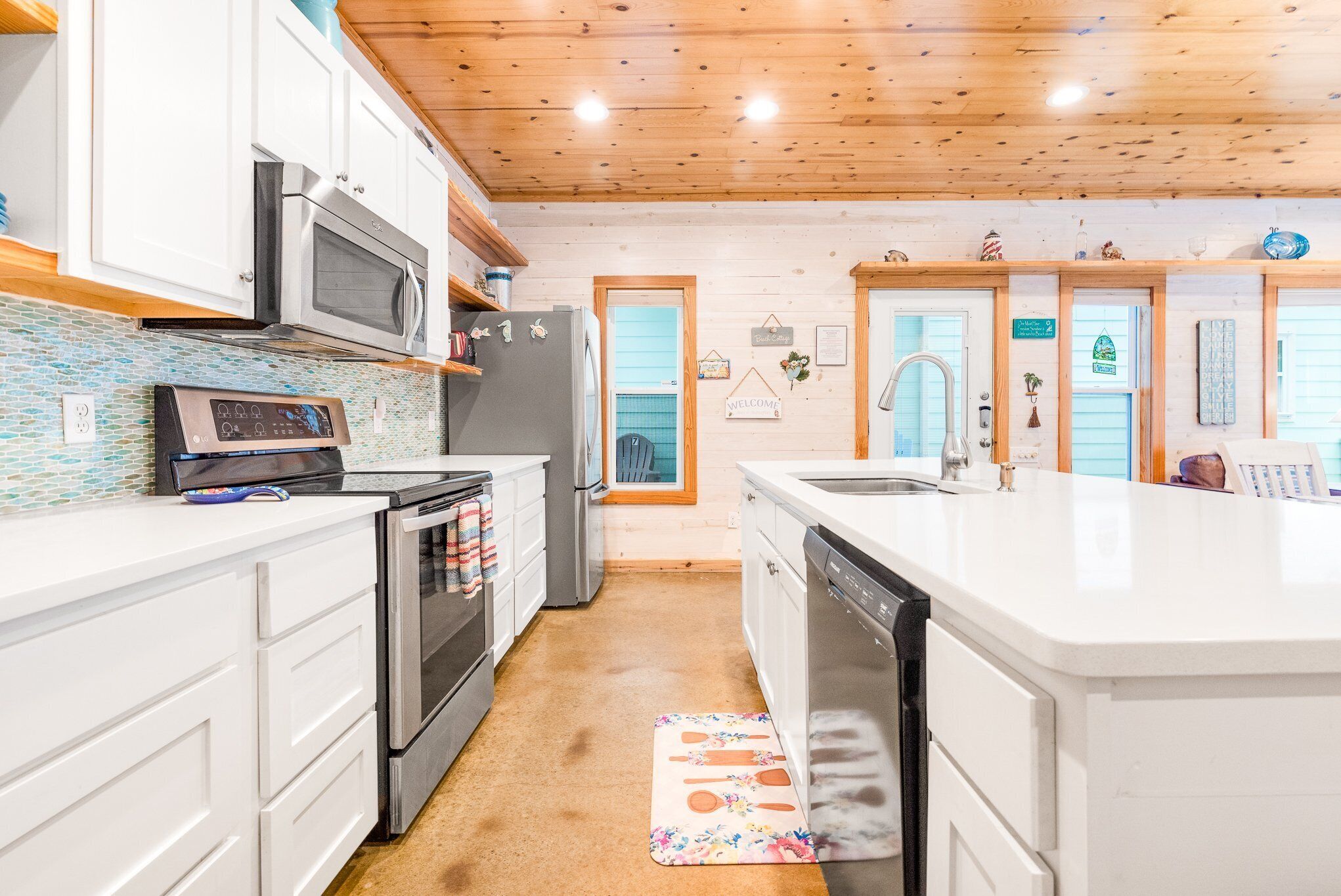 A modern kitchen with white cabinetry, stainless steel appliances, and a wooden ceiling.