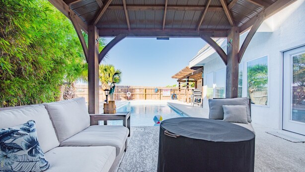 A covered outdoor seating area with a pool, a sofa, and a round table.