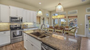 Una cocina moderna con encimeras de granito, electrodomésticos de acero inoxidable e iluminación colgante.